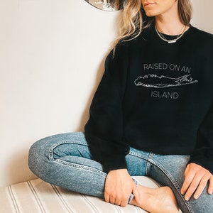 May include: Black sweatshirt with a white outline of Long Island and the text "RAISED ON AN ISLAND".