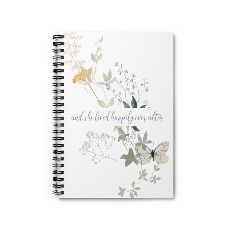 K&ouml;nnte beinhalten: Ein wei&szlig;es Spiralnotizbuch mit einem floralen Design und dem Text "and she lived happily ever after" in blauer Schrift. Die Blumen sind in Gelb-, Gr&uuml;n- und Blaut&ouml;nen gehalten.