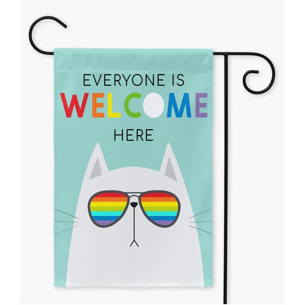 Może przedstawiać: Flaga ogrodowa z białym kotem w tęczowych okularach przeciwsłonecznych. Flaga ma jasnoniebieskie tło z napisem "Everyone is Welcome Here" w tęczowych literach.