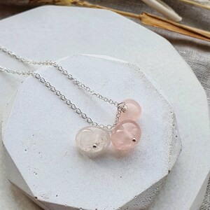 May include: A silver chain necklace with three pink rose quartz stones. The stones are oval shaped and have a natural, slightly cloudy appearance.