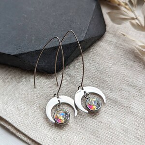 May include: Silver-tone crescent moon earrings with a dangling, iridescent, round crystal. The earrings have a long, curved hook design. The crystals reflect multiple colors, including pink, yellow, and blue.