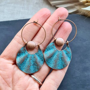Op de afbeelding: Een paar turquoise blauwe creolen met een getextureerd, golvend ontwerp. De creolen zijn gemaakt van koper en hebben een kleine koperen schijf in het midden van elke creool.