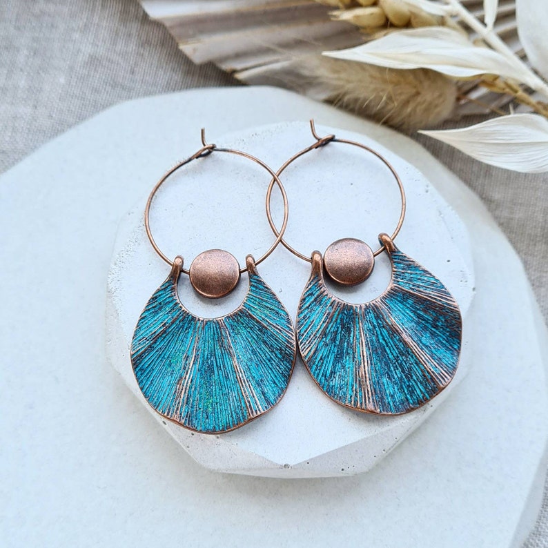 Op de afbeelding: Een paar koperen creolen met turquoise blauwe waaiervormige hangers. De oorbellen hebben een verweerde afwerking en een koperen kraal accent.