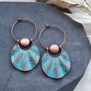 Op de afbeelding: Een paar koperen creolen met een turquoiseblauw, getextureerd, halve maan ontwerp. De oorbellen hebben een koperen kraal accent.