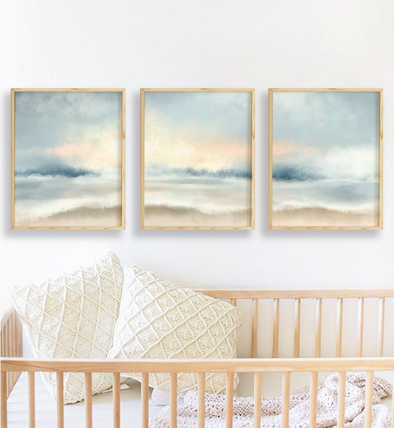 Pu&ograve; includere: Tre stampe artistiche incorniciate di paesaggi. Ogni stampa presenta una serena scena di spiaggia con un cielo azzurro chiaro, un tocco di pesca e una riva sabbiosa. L'opera d'arte &egrave; esposta sopra due cuscini decorativi color crema e una culla di legno.