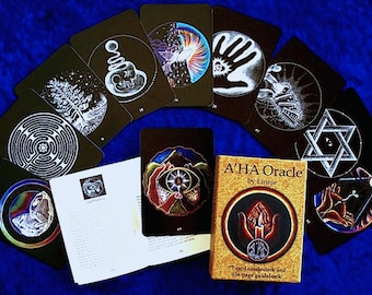 Op de afbeelding: Een zwart-wit orakelkaartendeck met een handleiding. De kaarten bevatten verschillende symbolen en ontwerpen, waaronder een labyrint, een boom, een hand, een ster en een oog. De handleiding is getiteld "A'HA Oracle by Linnie" en bevat een 77-kaarten orakeldeck en een 104-pagina handleiding.