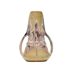 Può includere: Un vaso decorativo con una forma e un design unici. Il vaso presenta un colore di base beige chiaro con accenti rosa, neri e blu. Ha due manici curvi e una superficie strutturata. Il vaso è probabilmente realizzato in ceramica o terracotta.