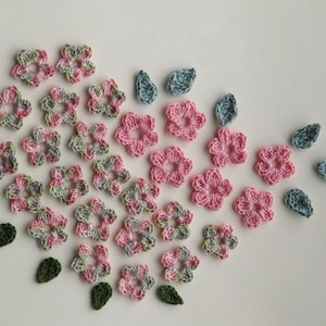 May include: A collection of crocheted flowers and leaves in shades of pink, green, and blue. The flowers are arranged in a heart shape.