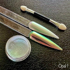 May include: A small jar of iridescent green and white nail polish pigment with two applicators and the word "Opal" written on the bottom of the image.