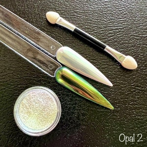 May include: A small jar of iridescent green and white glitter with two nail polish applicators and the text "Opal 2".