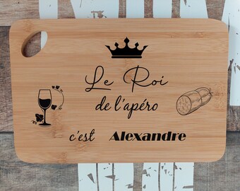 May include: A brown wooden cutting board with a black crown, a glass of wine, a sausage, and the text "Le Roi de l'apéro c'est Alexandre".