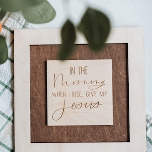 Pode incluir: Uma placa de madeira com uma moldura marrom clara e um fundo de madeira natural. A placa tem o texto "In the morning when I rise, give me Jesus" gravado em uma fonte cursiva.