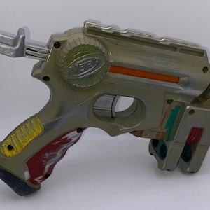 May include: A silver and green Nerf toy gun with a red and yellow grip. The gun has a silver barrel and a black trigger. The gun is made of plastic and has a Nerf logo on the side.