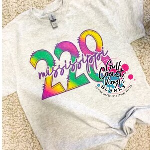 May include: A gray t-shirt with a colorful graphic that says "220 mississippi" in a rainbow gradient. The graphic has a jagged edge and is outlined in black. The text "Gulf Coast Vinyl & Blanks" is in the bottom right corner of the image.
