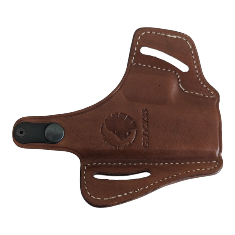 May include: A brown leather holster with white stitching. The holster has a black snap closure and a logo with a bison head. The text "GLOCK 43" is visible on the side.