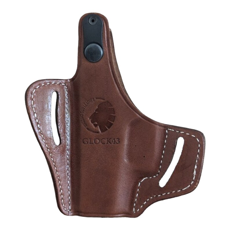 May include: A brown leather holster with white stitching and a black snap closure. The holster has cutouts and a logo with the text "GLOCK43". The holster is designed to hold a firearm.