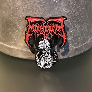 May include: Black and red metal pin with the word "Suffocation" in a gothic font. A black and white illustration of a skull with a flower in its eye socket is below the word.