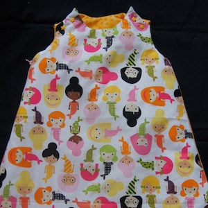 May include: A white sleeping bag with a colorful pattern of mermaids. The sleeping bag has a yellow and orange polka dot lining.