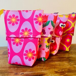 Peut inclure: Trois trousses à crayons verticales avec des designs télescopiques. La trousse au premier plan présente un motif ovale rose vif et lavande avec des fleurs au centre orange. La trousse du milieu affiche un imprimé floral et celle du fond un motif géométrique coloré avec un hibou stylisé.