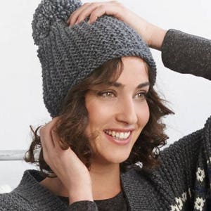 Peut inclure: Un bonnet en tricot gris avec un pompon moelleux sur le dessus. Le bonnet est réalisé avec un point texturé.