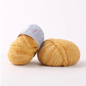 May include: Two balls of yellow yarn with a white label that reads "Phildar Phil Nature" and has information about the yarn.