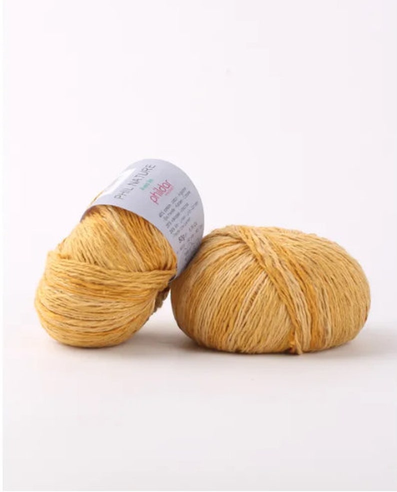 May include: Two balls of yellow yarn with a white label that reads "Phildar Phil Nature" and has information about the yarn.