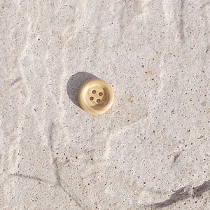 Könnte beinhalten: Ein hellbrauner Holz-Knopf mit vier Löchern.