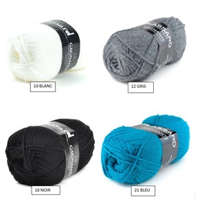 May include: Four balls of yarn in white, grey, black, and teal. Each ball has a label with the brand name and colour number. The white ball is labelled "10 BLANC", the grey ball is labelled "12 GRIS", the black ball is labelled "16 NOIR", and the teal ball is labelled "21 BLEU".