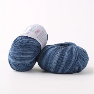 May include: Two balls of blue yarn with a white label that reads "Phil Nature" and "Phildar" in pink lettering. The label also includes information about the yarn's composition and care instructions.