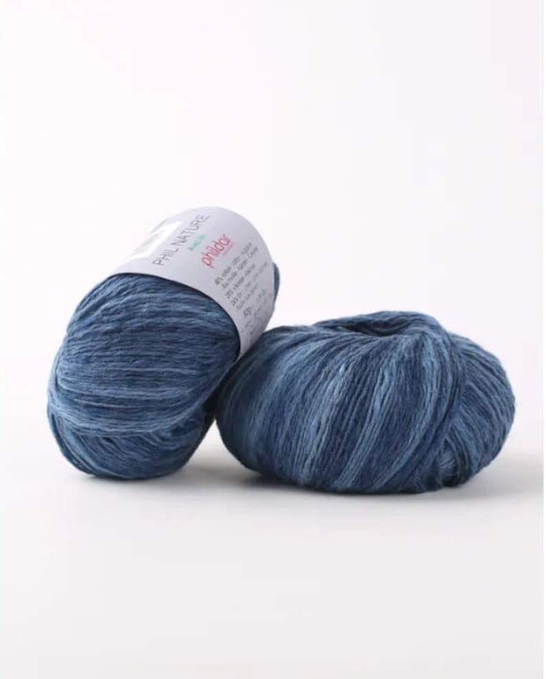May include: Two balls of blue yarn with a white label that reads "Phil Nature" and "Phildar" in pink lettering. The label also includes information about the yarn's composition and care instructions.