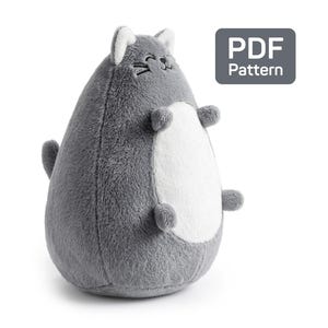 Puede incluir: Un juguete de peluche gris con forma de gato, con vientre blanco y pequeños brazos y piernas. El gato tiene una cara sonriente con detalles bordados en negro. El juguete tiene una etiqueta de patrón PDF. Es un juguete suave y tierno.