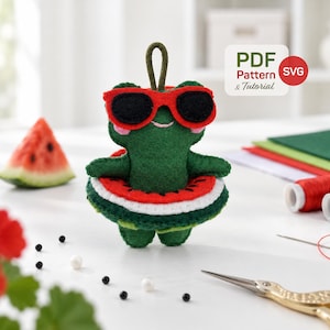 Pode incluir: Um enfeite de sapo em feltro verde usando óculos de sol com armação vermelha e uma boia com estampa de melancia. O sapo possui uma alça para pendurar e detalhes bordados. O texto na imagem diz PDF Pattern & Tutorial SVG.