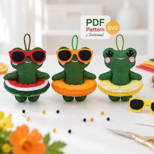 Op de afbeelding: Drie groene viltkikker-ornamenten met ophanglussen, elk met een zonnebril en een fruitvormige zwemband. De kikkers hebben rode, oranje en gele accenten. Een wit label toont de tekst PDF Pattern & Tutorial en SVG.