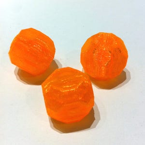 May include: Three bright orange, geometric, multi-faceted objects are arranged on a white surface. The objects have a textured appearance, with visible layering. The lighting creates shadows, enhancing the three-dimensional effect of the shapes.
