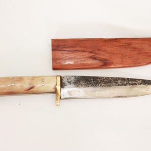 May include: A knife with a bone handle and a metal blade. The knife is in a wooden sheath.