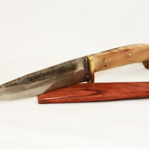May include: A handmade knife with a bone handle and a brass bolster. The blade is made of steel and has a dark patina. The knife comes with a wooden sheath.