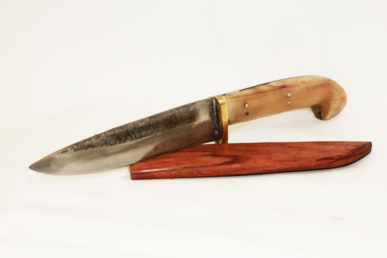 May include: A handmade knife with a bone handle and a brass bolster. The blade is made of steel and has a dark patina. The knife comes with a wooden sheath.