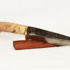 May include: A handcrafted knife with a bone handle and a dark metal blade. The knife is resting on a wooden sheath.