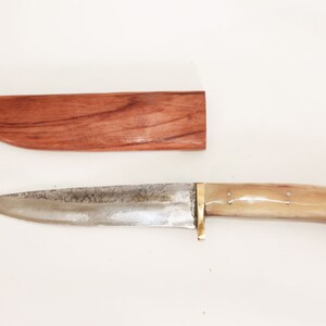 May include: A silver knife with a bone handle and a wooden sheath. The knife has a brass guard and a slightly curved blade.
