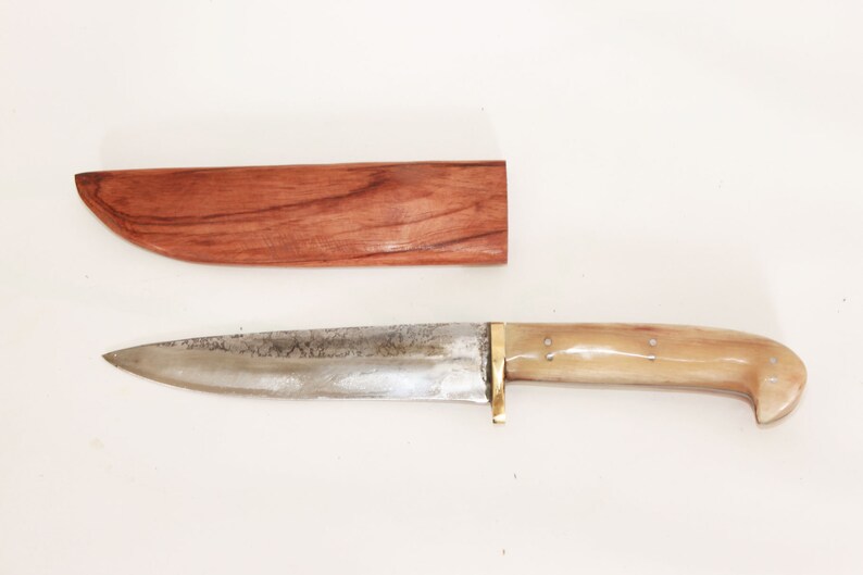 May include: A silver knife with a bone handle and a wooden sheath. The knife has a brass guard and a slightly curved blade.