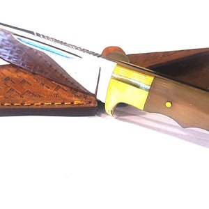 May include: A brown leather sheath with a stitched edge holds a hunting knife with a brown handle and a silver blade.