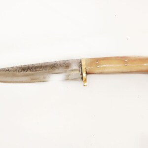 May include: A vintage hunting knife with a bone handle and a brass guard. The blade is made of steel and has a slight curve.