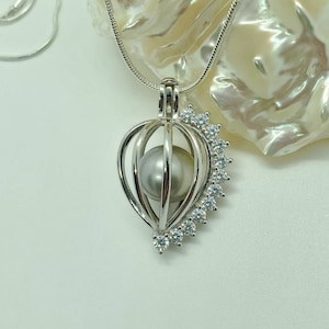 May include: A silver pearl cage necklace with a white pearl inside and a row of clear cubic zirconia stones around the cage.