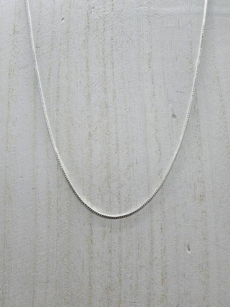 May include: A silver chain necklace on a white wooden background.