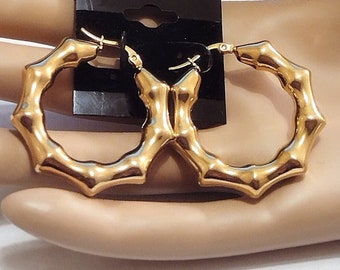 May include: Gold hoop earrings with a bamboo-like design. The earrings are large and have a shiny finish.