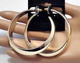 May include: A pair of large, gold-toned hoop earrings. The earrings are thick and have a smooth, polished finish.