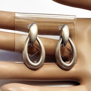May include: A pair of silver dangle earrings with a unique oval shape. The earrings have a simple design and are perfect for everyday wear.