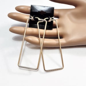 May include: A pair of gold-toned rectangular hoop earrings. The earrings are simple and modern in design.