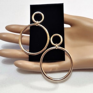 May include: A pair of gold hoop earrings with a smaller circle attached to the larger circle.