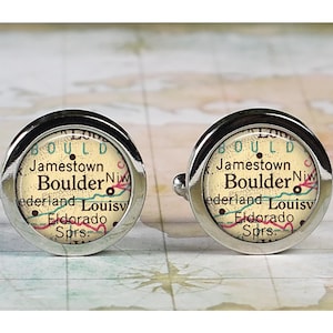 May include: A pair of silver cufflinks with a vintage map design featuring the text "BOULD Jamestown Boulder Niw ederland Louisv Eldorado Sprs."